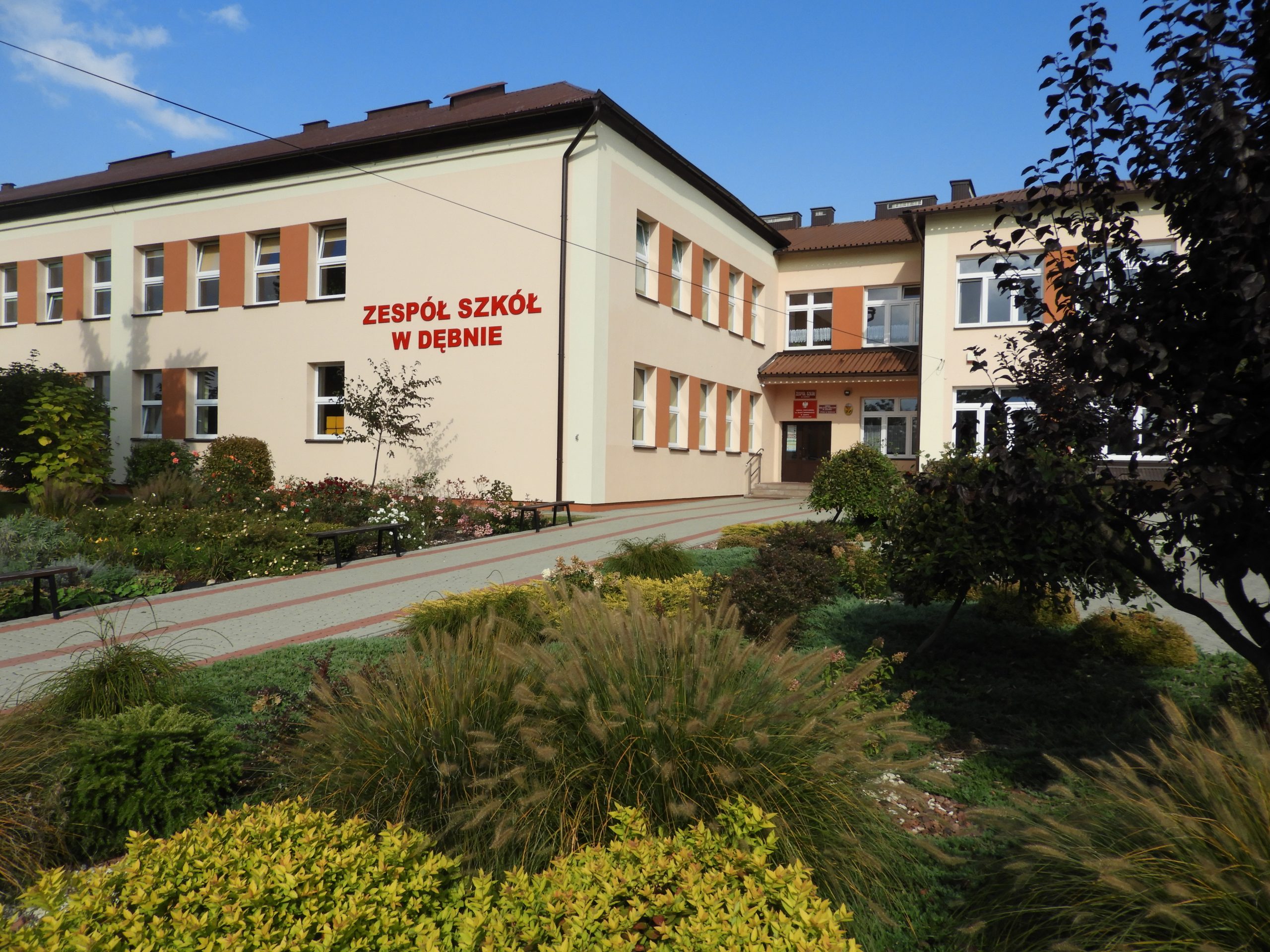 Budynek zespołu szkół w Dębnie widziany od wejścia głównego, przed budynkiem rabaty z krzewami.