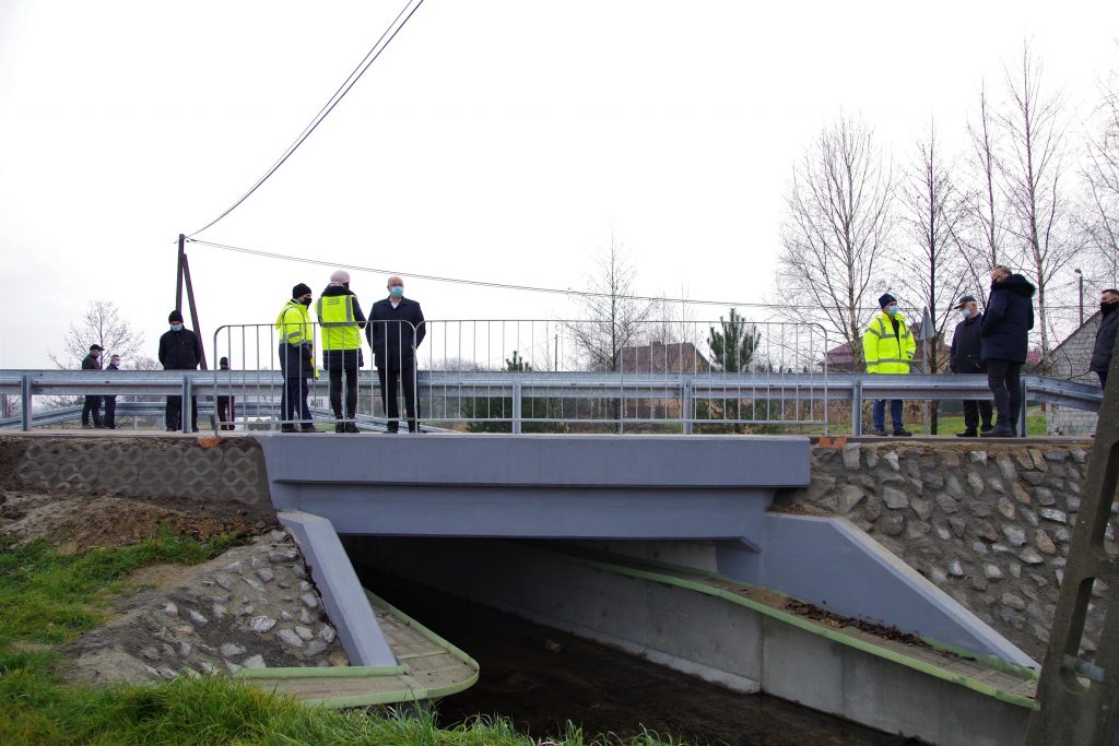 Kolejny mostek na przebudowanej drodze. Po obu stronach wzmocniony kamieniami. Na mostku stoją inwestorzy i wykonawcy inwestycji.