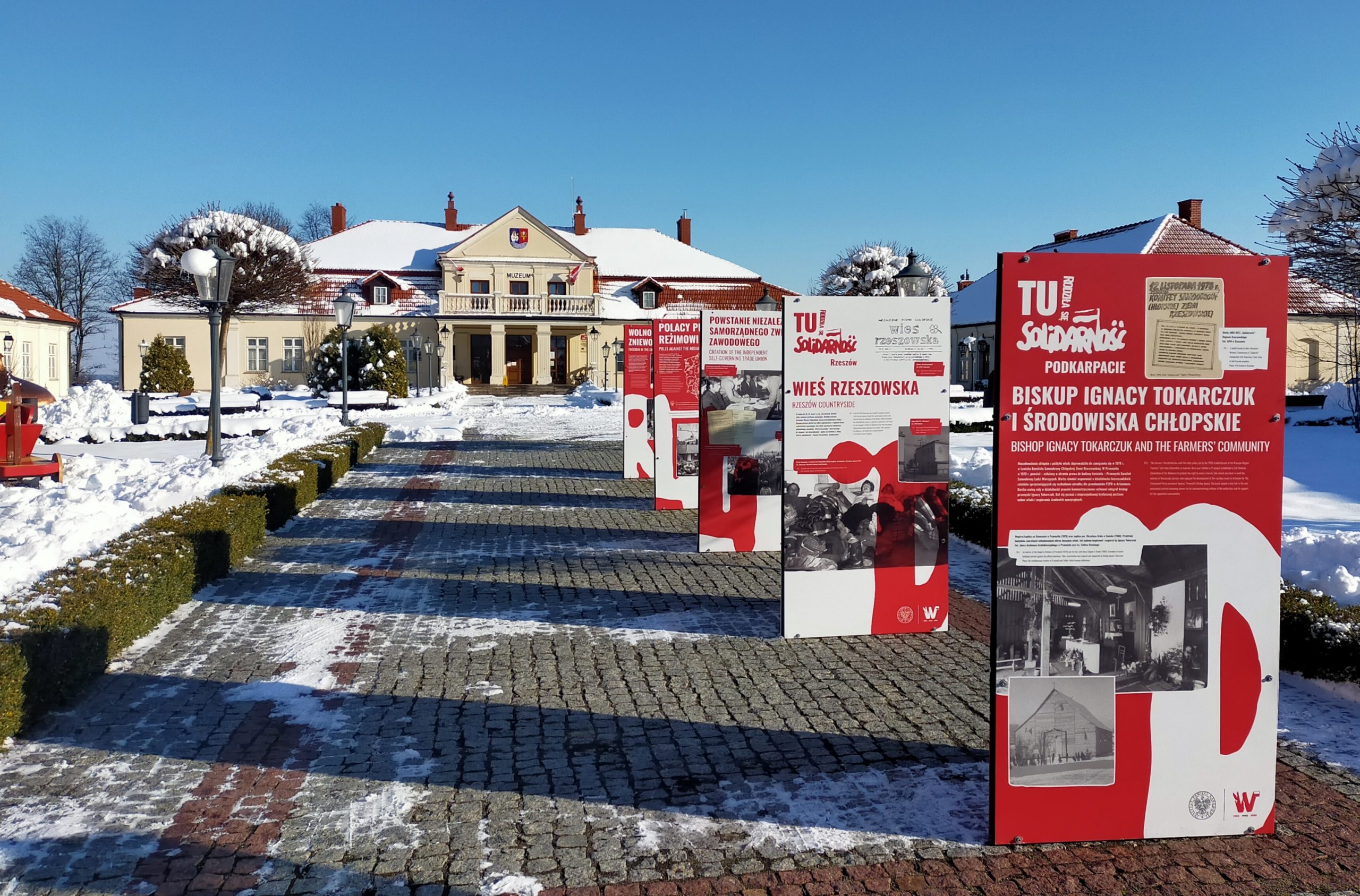 Czerwone plansze z białymi napisami oraz czarno-białymi zdjęciami przedstawiające chronologicznie wydarzenia związane z tematyką wystawy. Plansze ustawione są wzdłuż chodnika prowadzącego do głuwnego wejścia muzeum od strony ulicy Mickiewicza. W tle budynek muzeum.