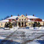 Front budynku muzeum w ośnieżonej scenerii w słoneczny dzień. Główne wejście zdobią cztery filary, nad nimi znajduje się taras widokowy, zaś na fasadzie nad wejściem głównym widnieje herb powiatu. Przed budynkiem po obu stronach znajdują się krzewy i oraz niewielkie drzewa.