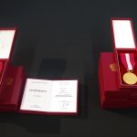 Dwa medale złoty i srebrny w bordowych pudełkach leżące na stole przykrytym ciemnozieloną tkaniną