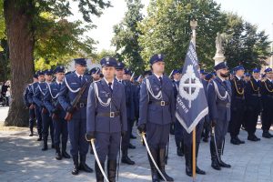 Kompania honorowa oddziału służby więziennej stojąca w szyku na placu przed sanktuarium przodem do ołtarza. Jeden ze strażników trzyma sztandar.